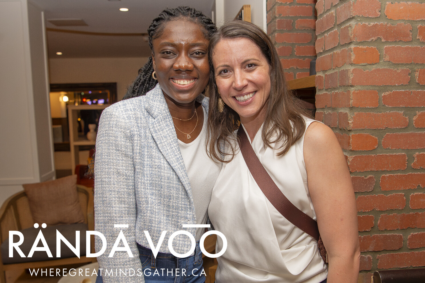 Two guests smiling beside an exposed brick wall.