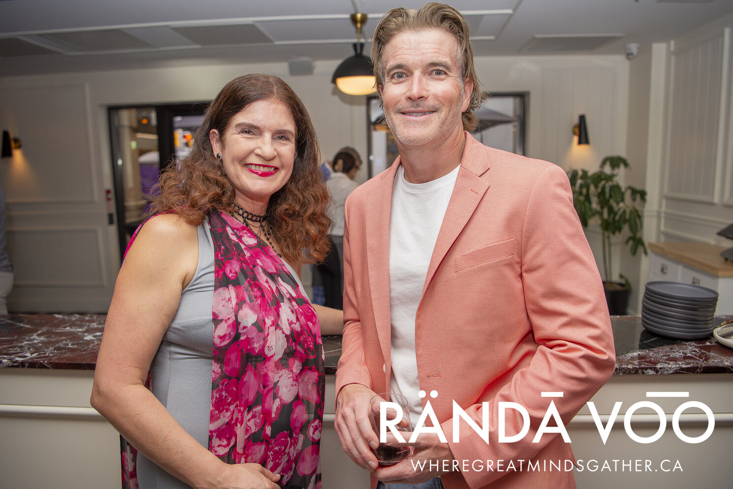Two guests smiling beside the bar, one wearing a coral jacket.