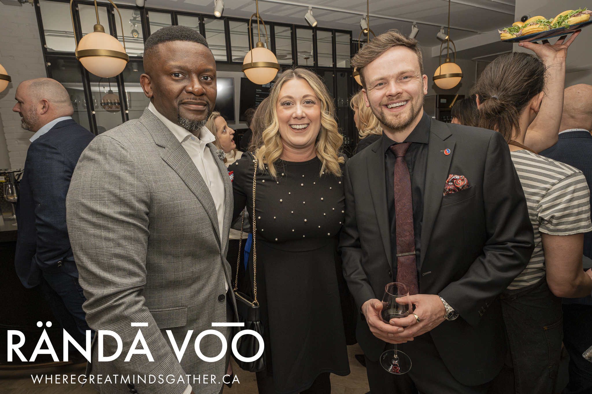 Three guests smiling together beneath pendant lights at the wine-tasting gathering.