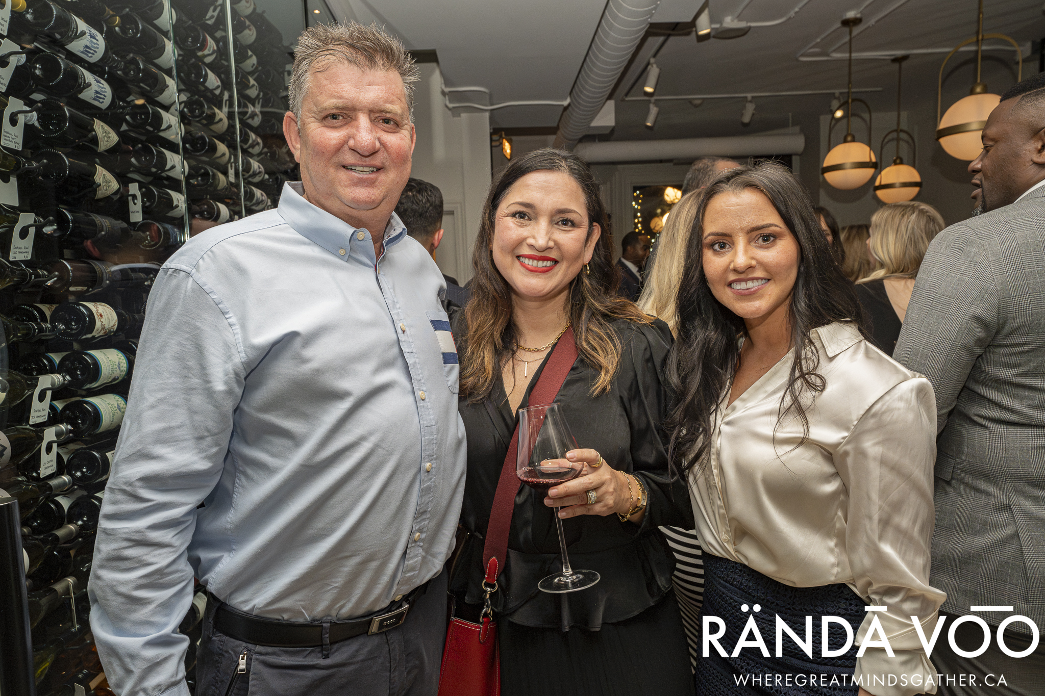 Three guests posing beside the glass wine display at the Prestige reception.