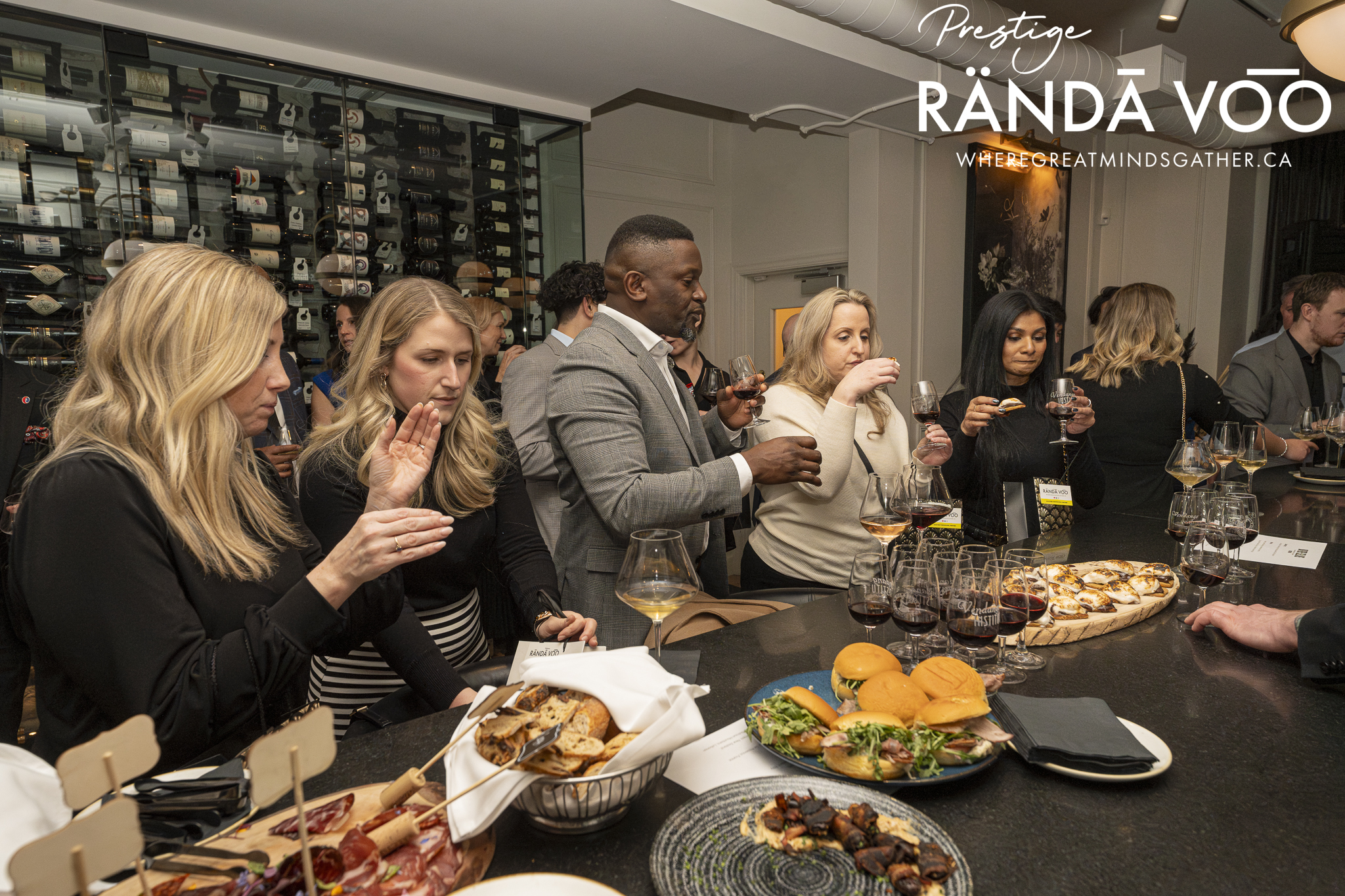 Guests enjoying wine and food pairings around the counter at a RÄNDĀ VO͞O Prestige gathering.