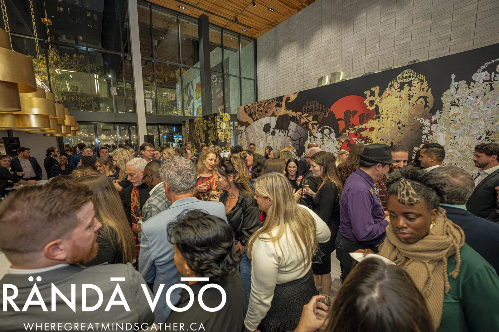 Guests gathered for a RÄNDĀ VO͞O reception beneath a wood ceiling beside a colourful large-scale wall mural.