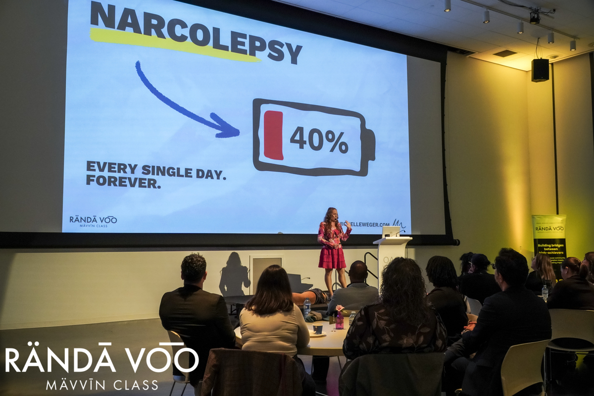 Michelle Weger presenting beside a slide showing a battery at 40 percent, with guests seated in the audience.