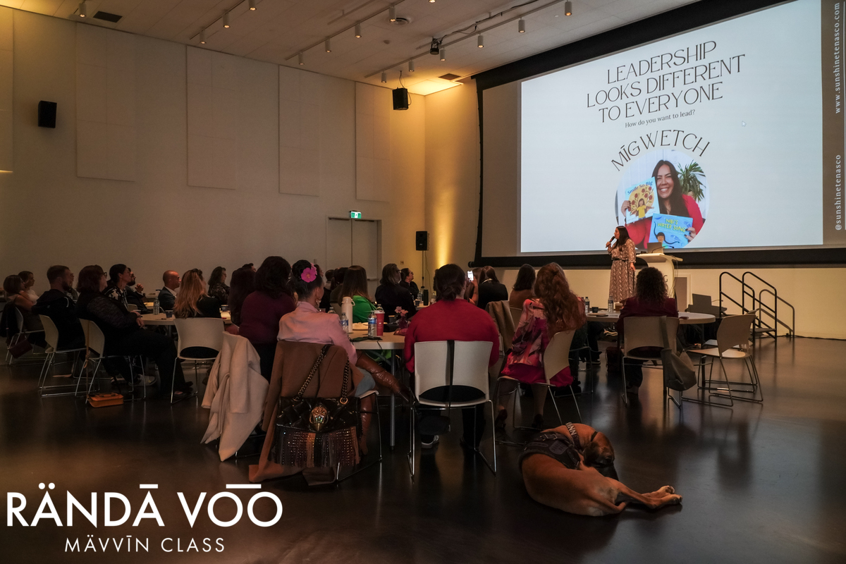 A wide view of Sunshine Tenasco presenting to seated guests at MÄVVĪNCLASS The Capacity Room.