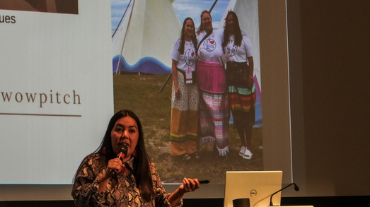 Sunshine Tenasco speaking into a microphone beside the presentation screen at The Capacity Room.