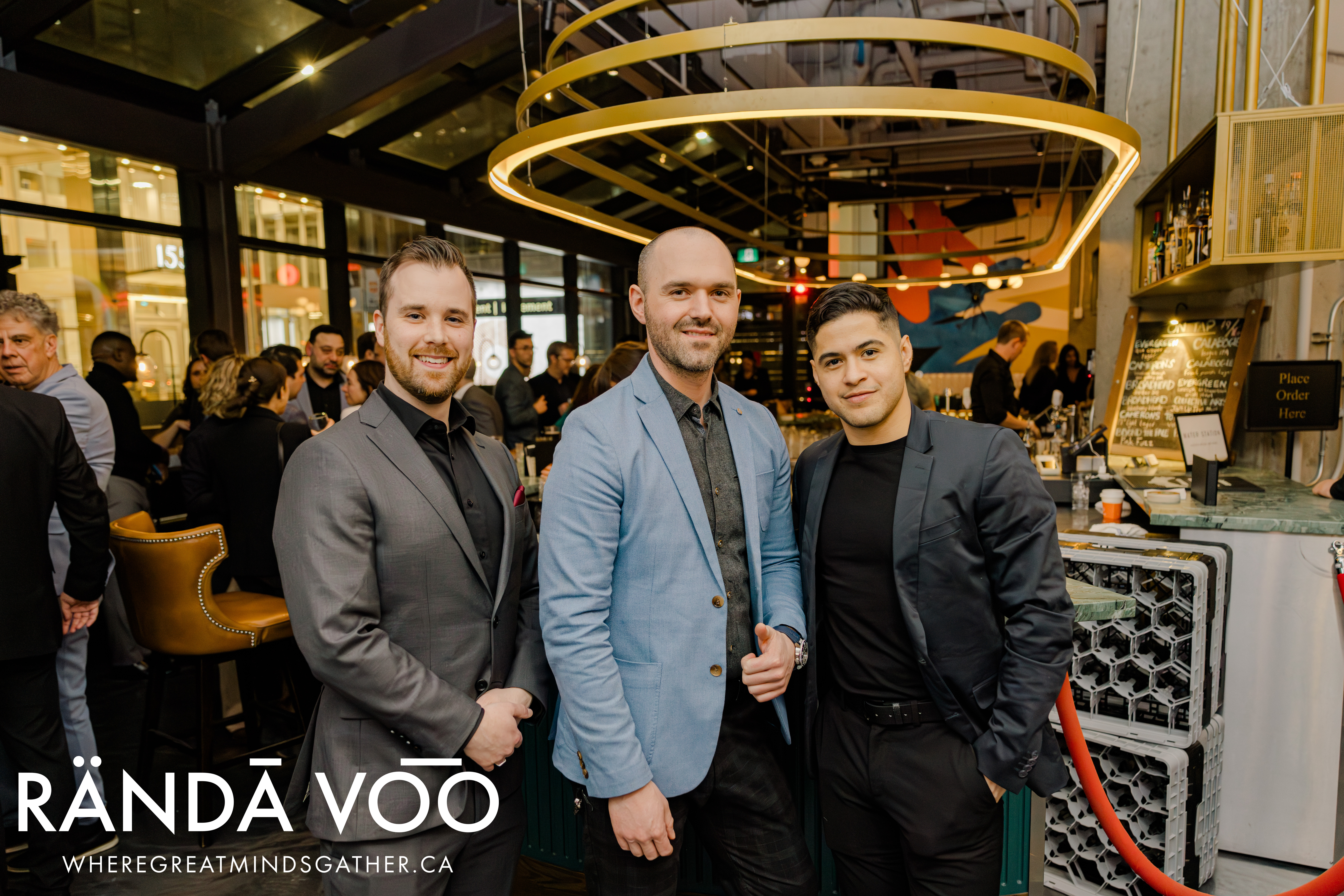 Three guests gathered beneath circular lights at Queen St. Fare, with RÄNDĀ VO͞O branding.