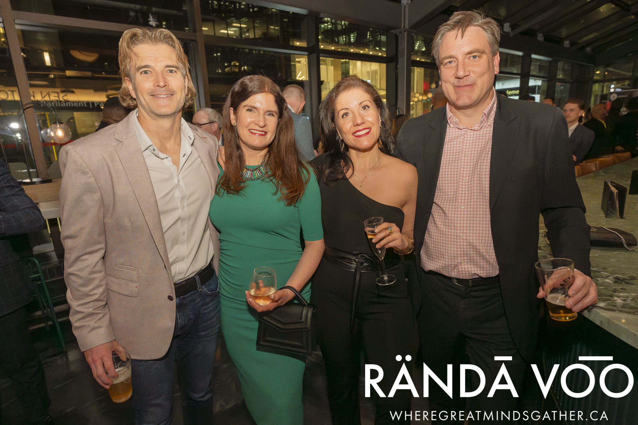 Four guests posing together beside the windows, with RÄNDĀ VO͞O branding.