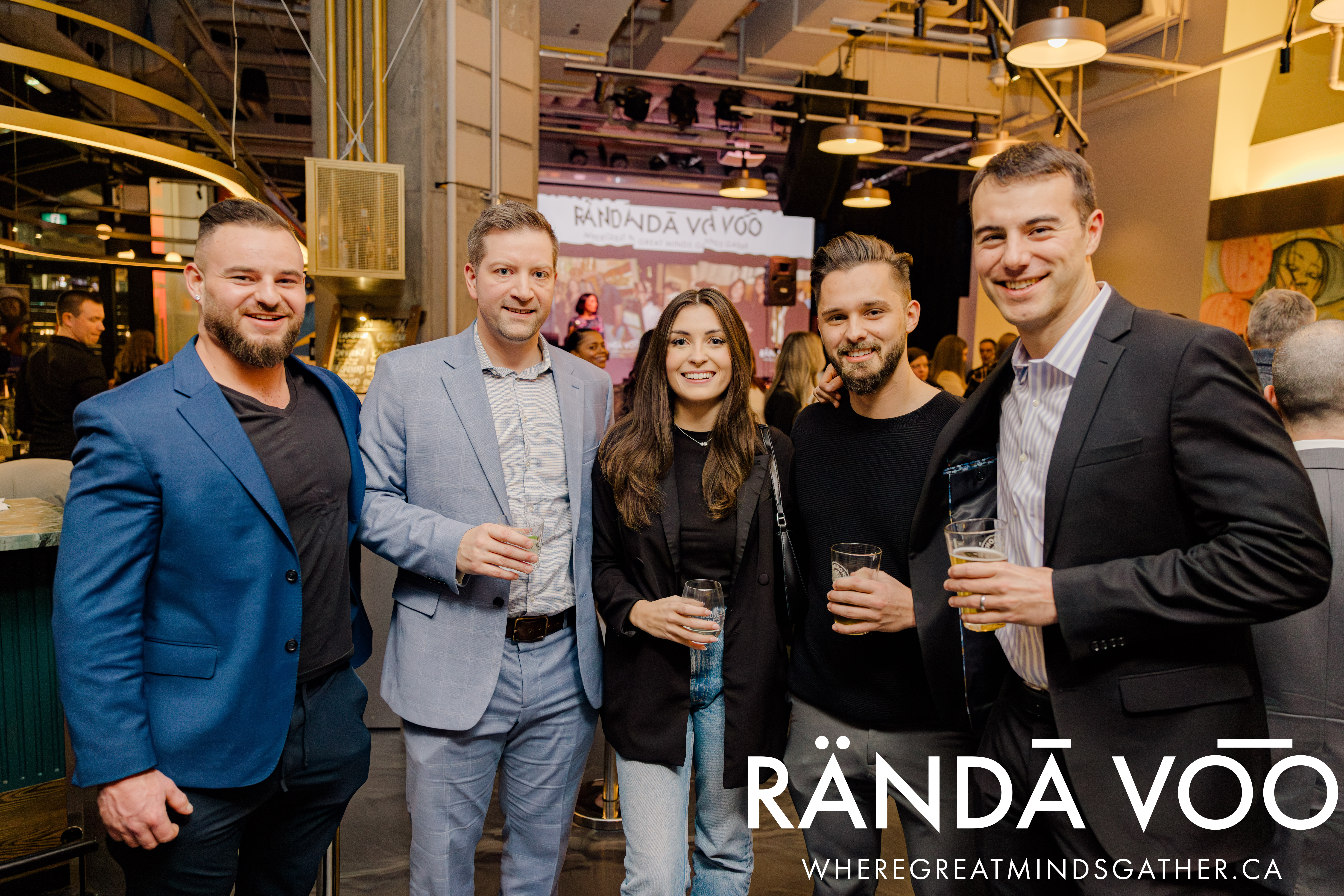 Five guests gathered at Queen St. Fare with the event stage behind them and RÄNDĀ VO͞O branding.