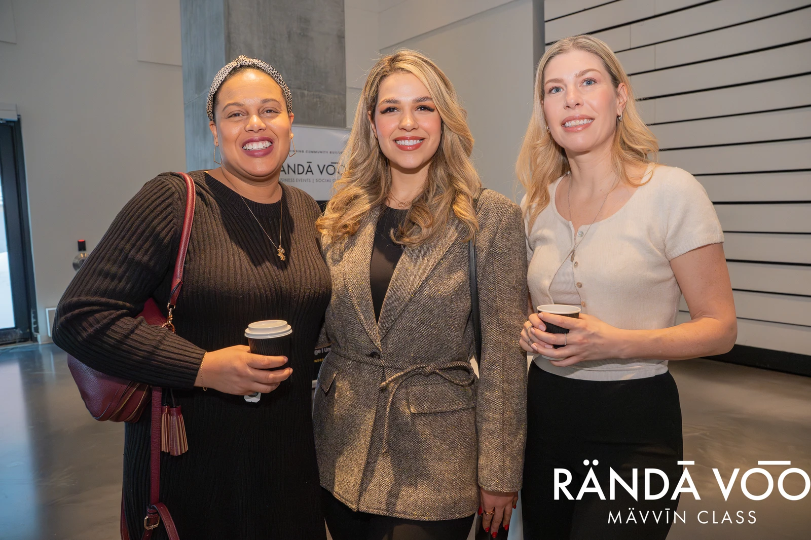 Three RÄNDĀ VO͞O business community attendees with coffee cups at a MÄVVĪNCLASS gathering.