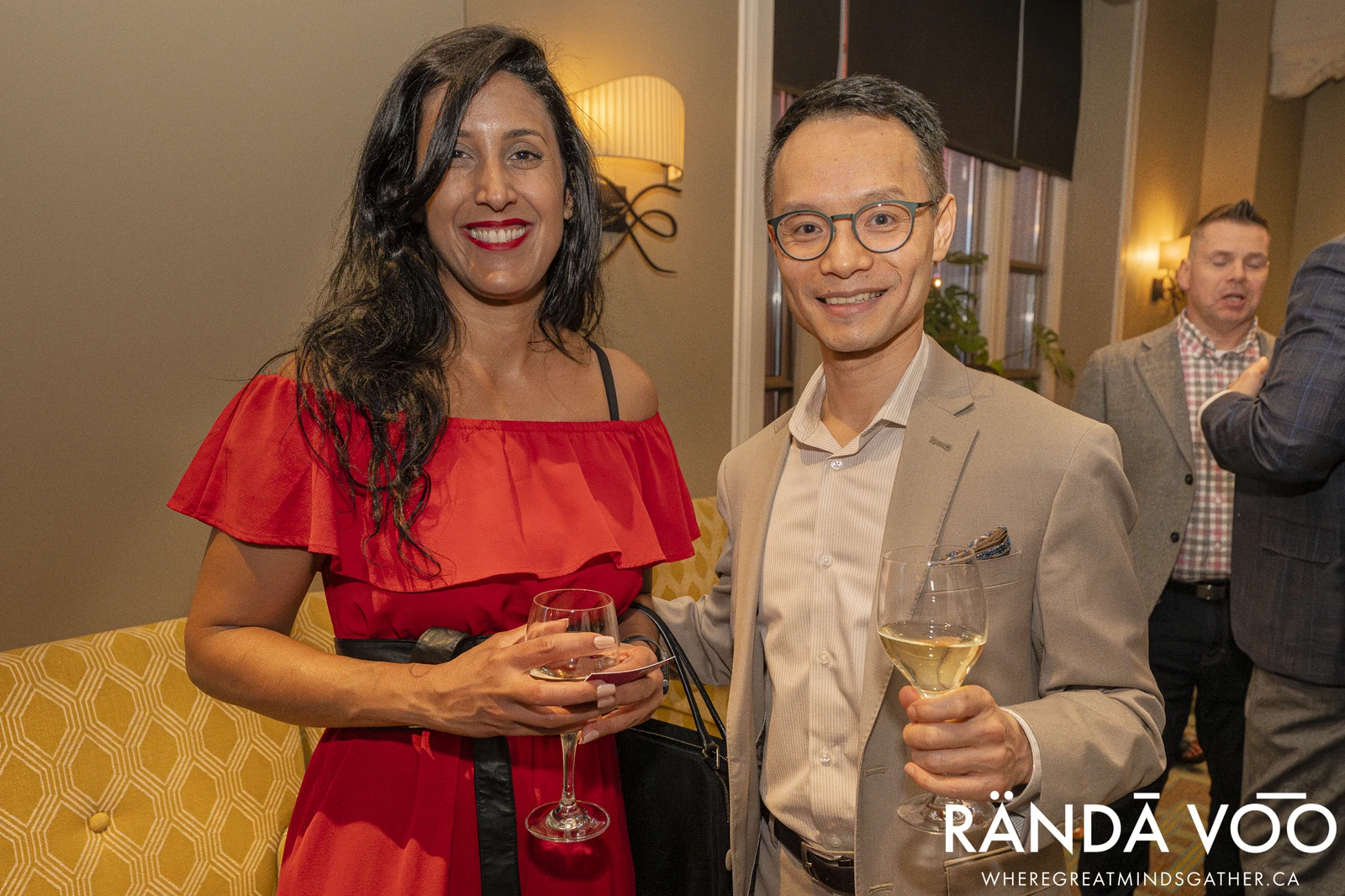 Two attendees posing with drinks at a RÄNDĀ VO͞O business community evening gathering.