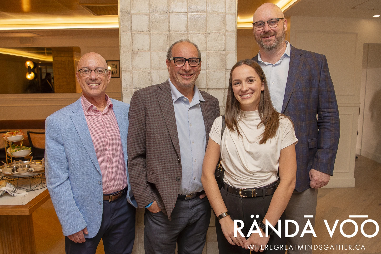 Four attendees posing together beside a reception buffet at a RÄNDĀ VO͞O business community gathering.