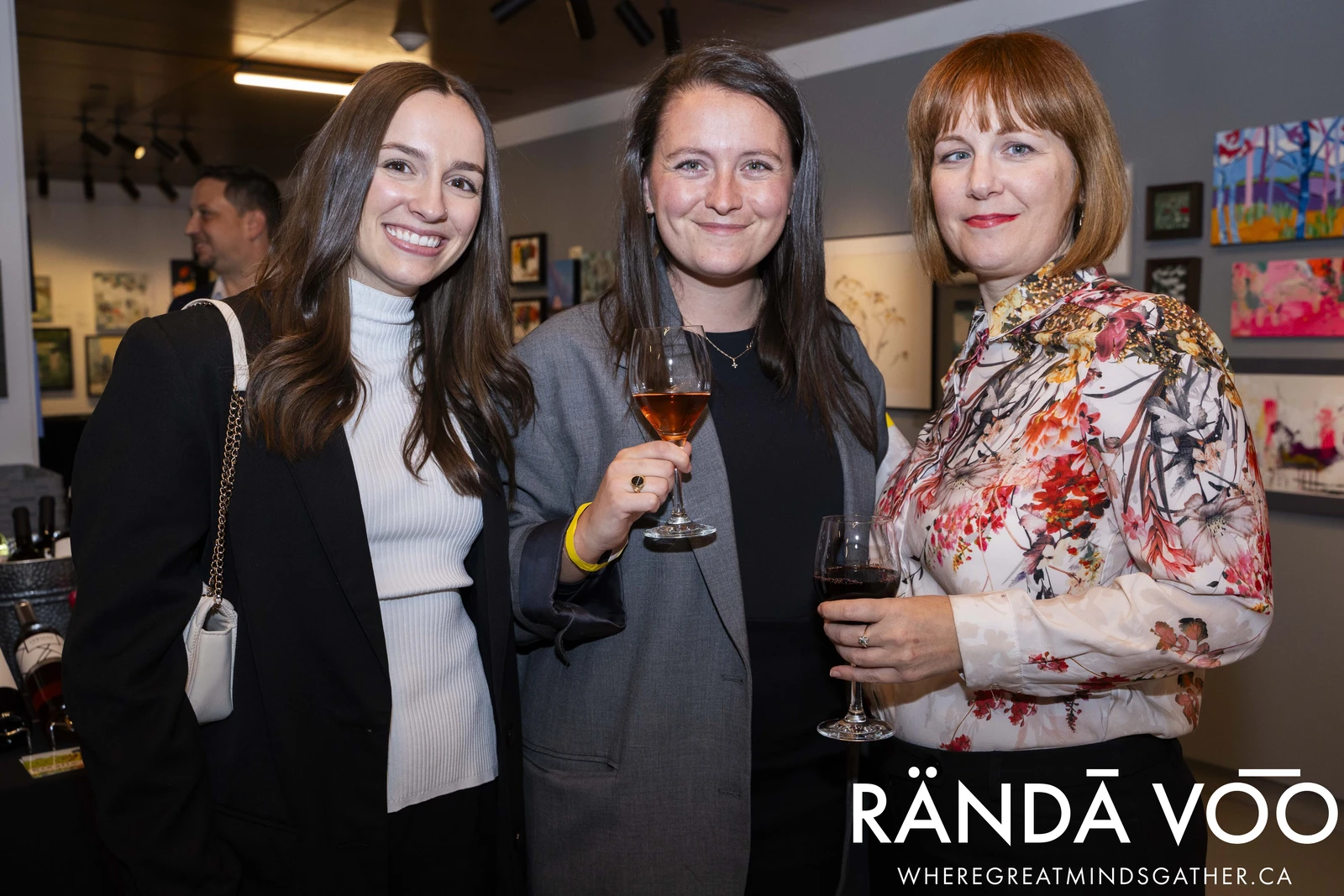 Three attendees posing together with artwork displayed behind them at a RÄNDĀ VO͞O business community gathering.
