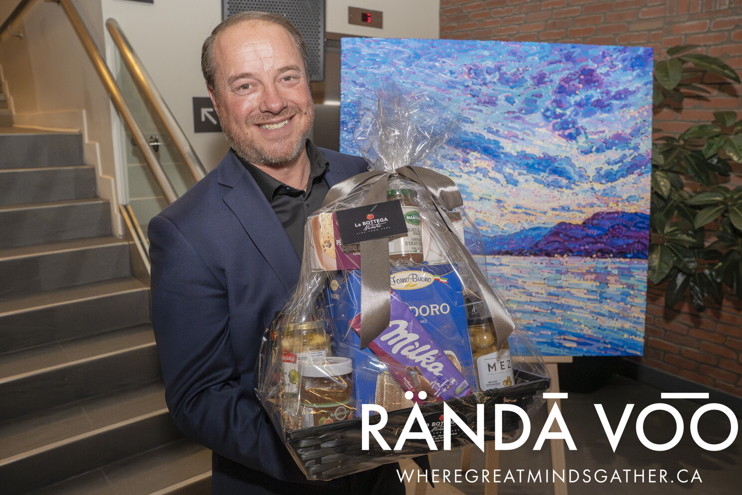 A guest holding a La Bottega gift basket beside a colourful painting.