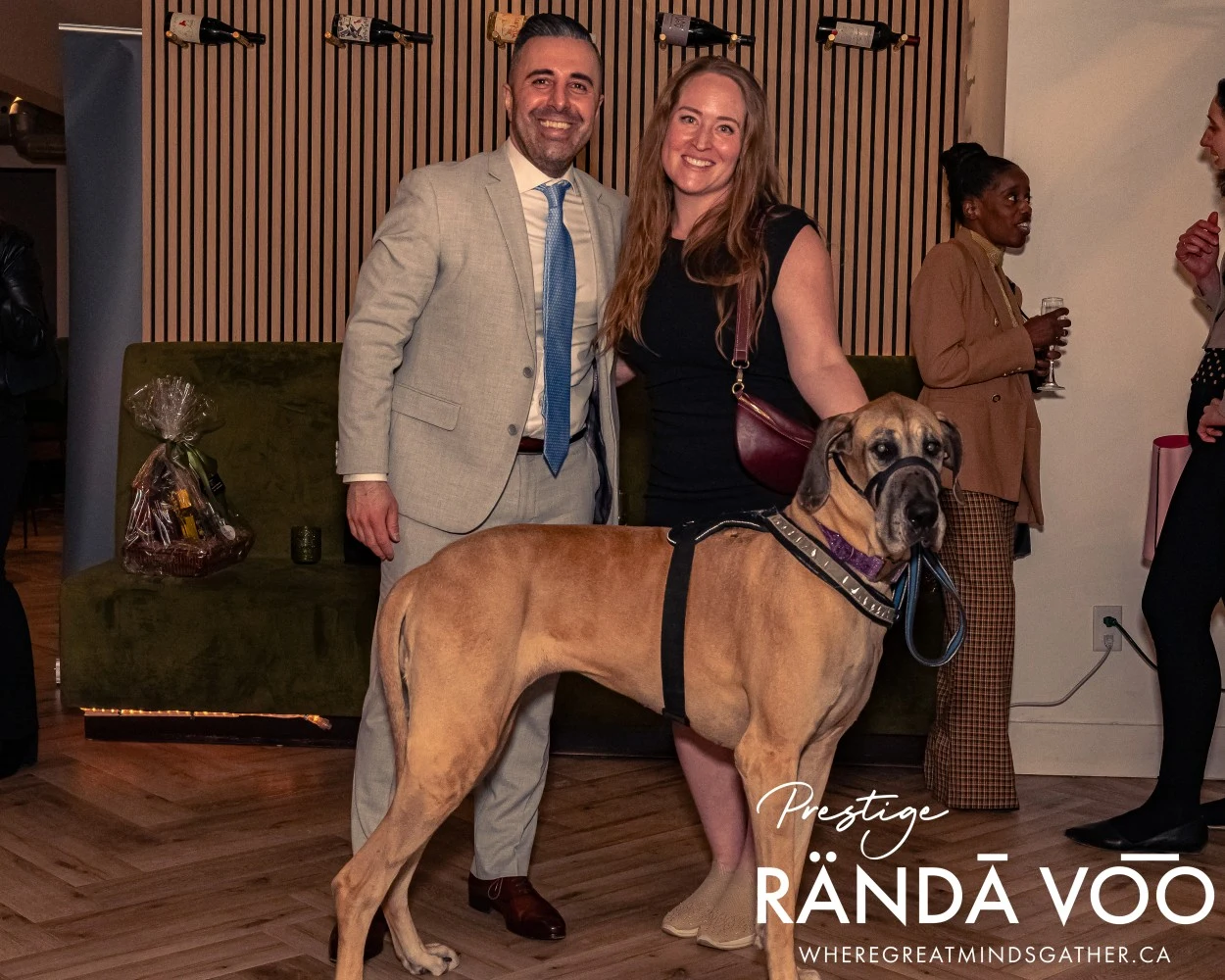 Two guests posing with a large dog at HEIST Manotick, with RÄNDĀ VO͞O Prestige branding.