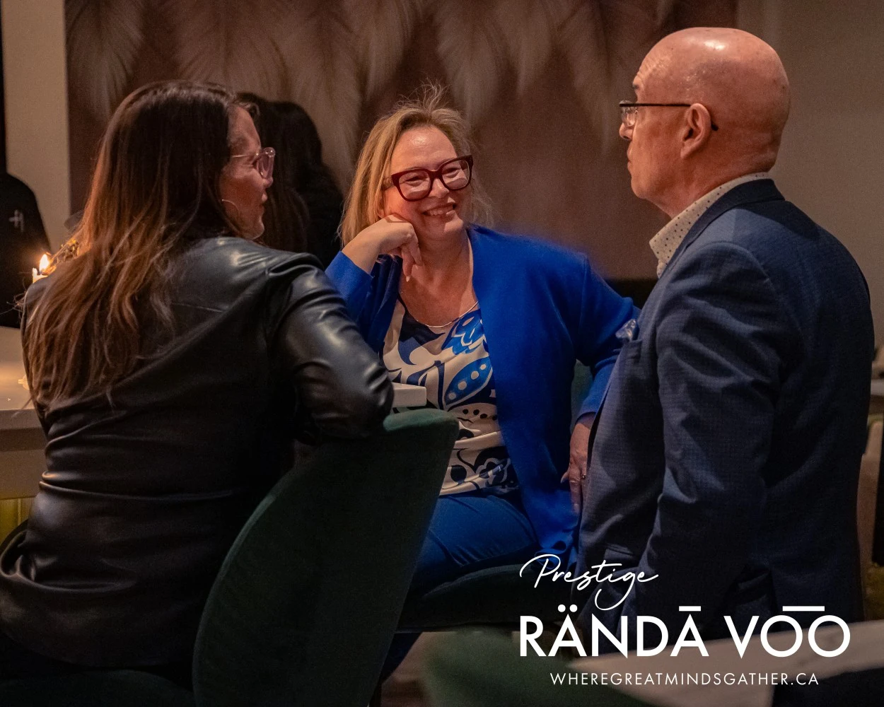 Three guests in conversation at HEIST Manotick, with RÄNDĀ VO͞O Prestige branding.
