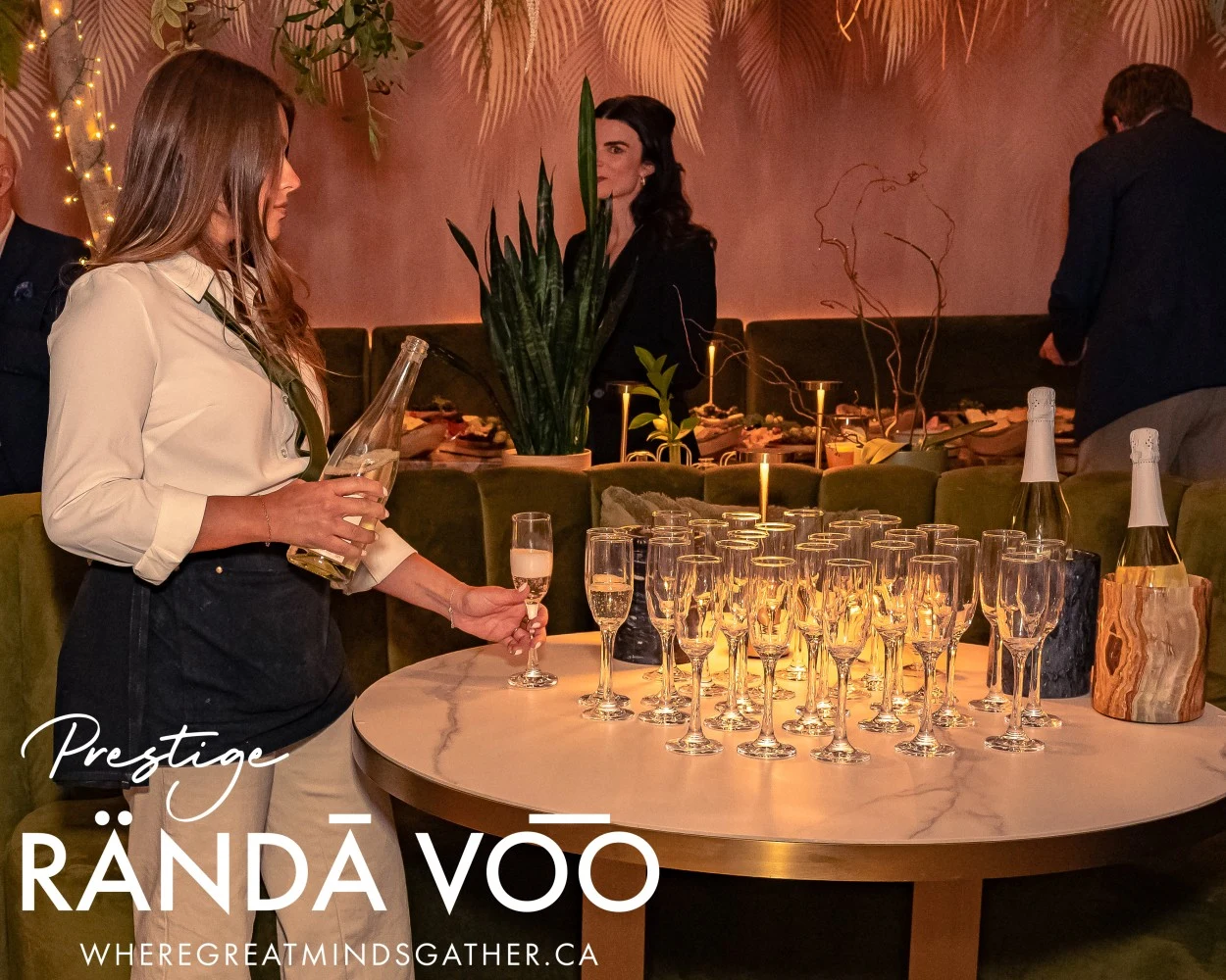 A server preparing glasses of sparkling wine at HEIST Manotick, with RÄNDĀ VO͞O Prestige branding.