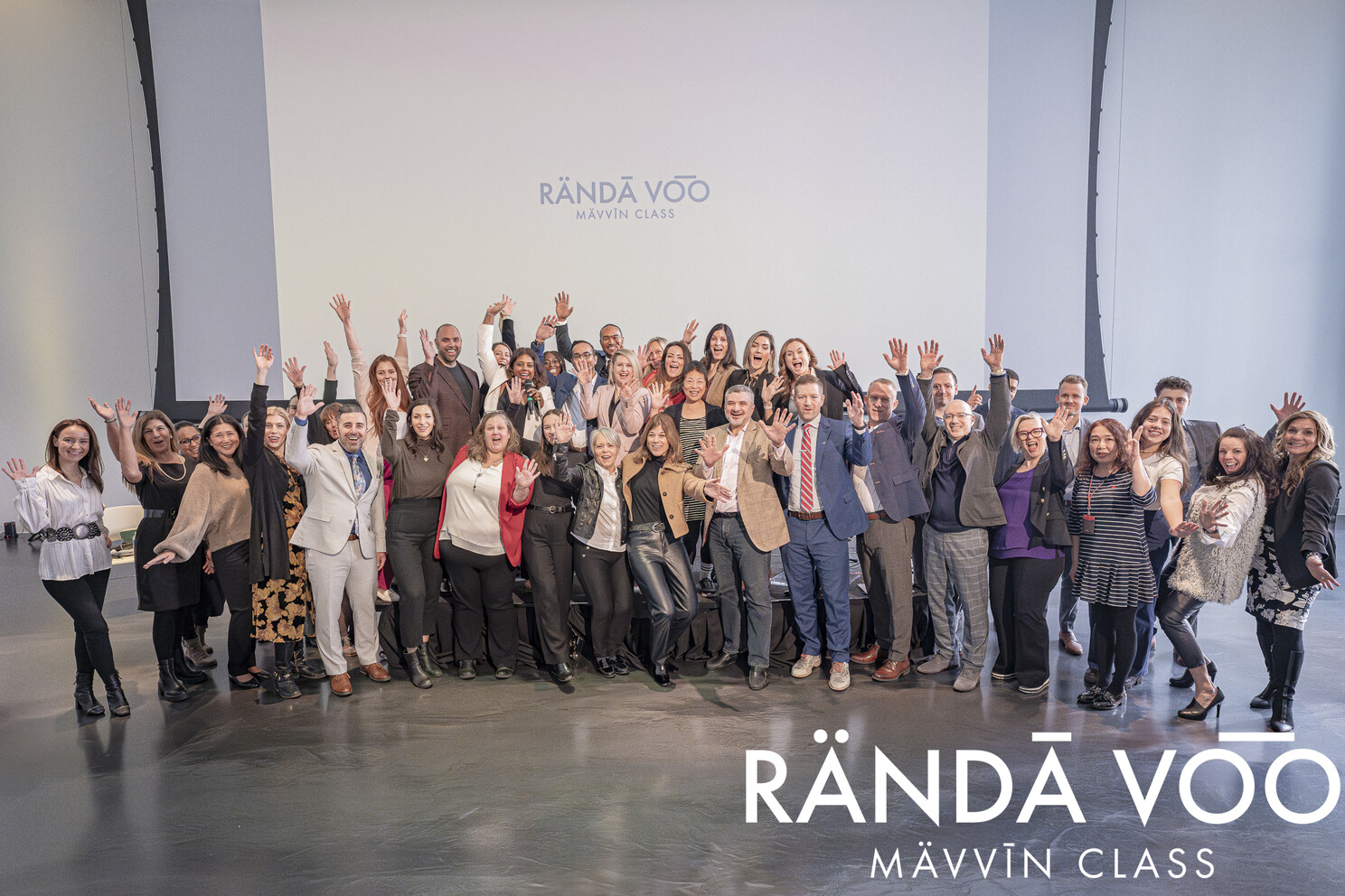 MÄVVĪNCLASS participants waving for a group photo beneath the projected RÄNDĀ VO͞O logo.