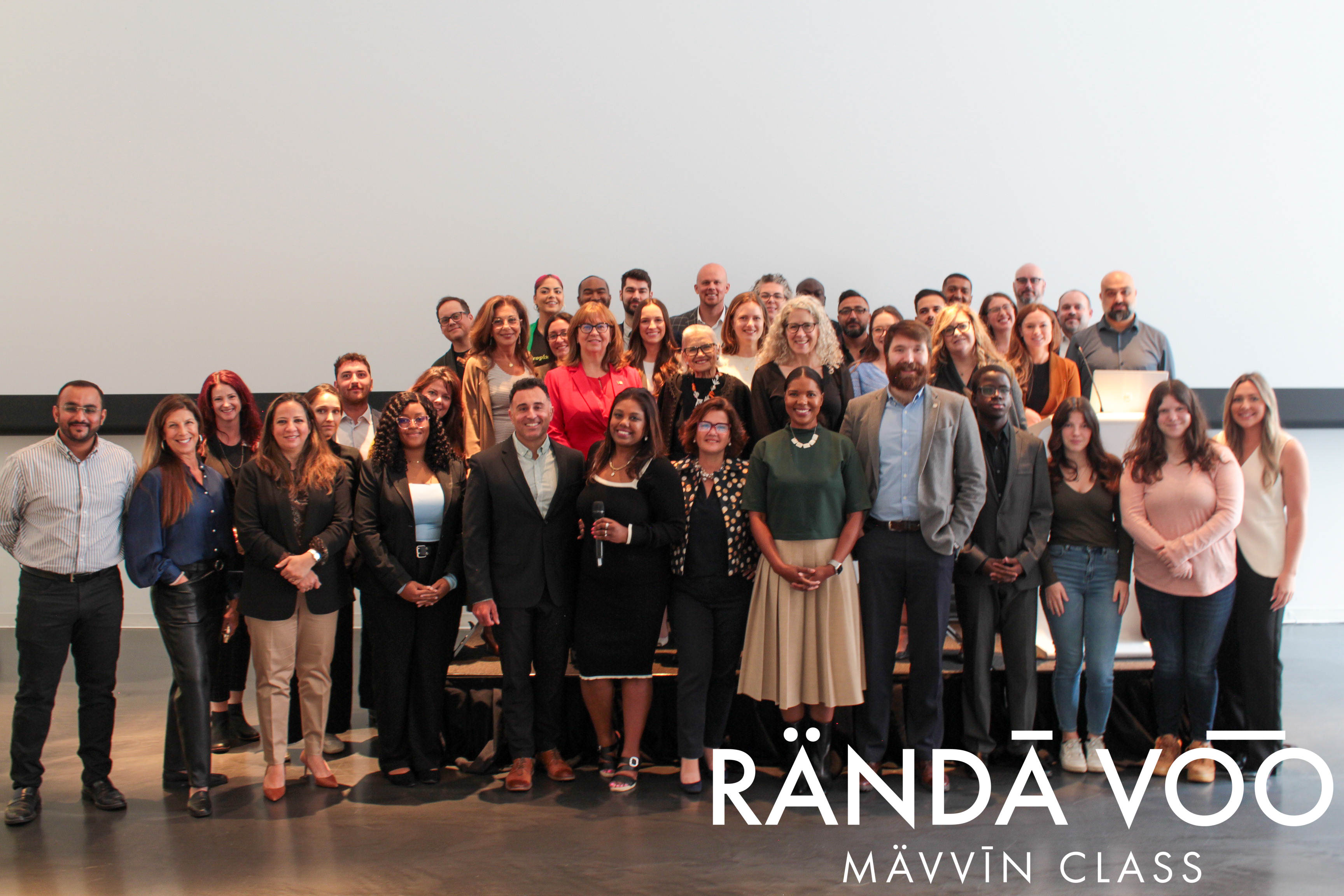 MÄVVĪNCLASS participants waving together for a group photo in front of the Brazeau Seller Law projection.