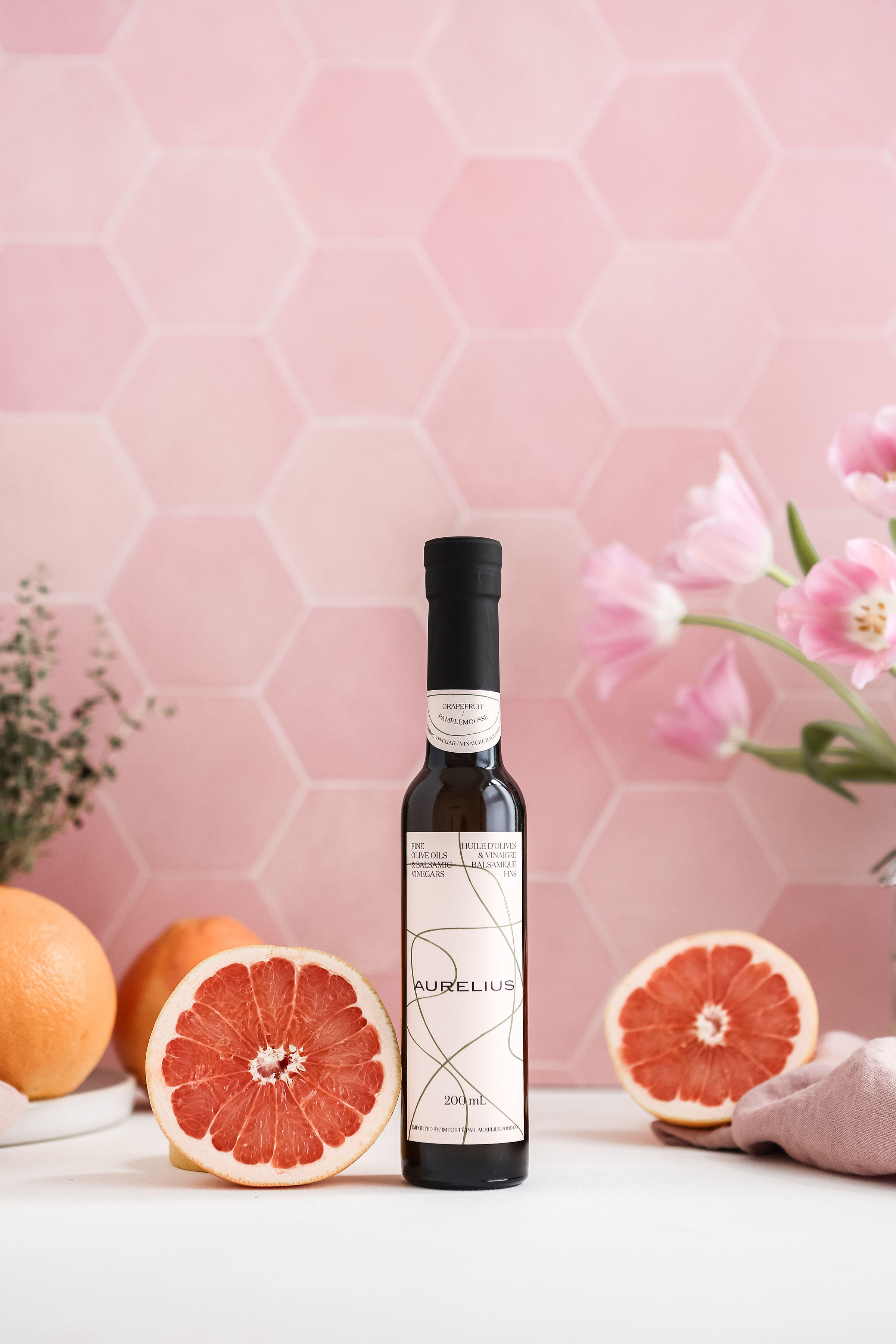 An Aurelius bottle arranged beside fresh grapefruit against a pink tiled backdrop.