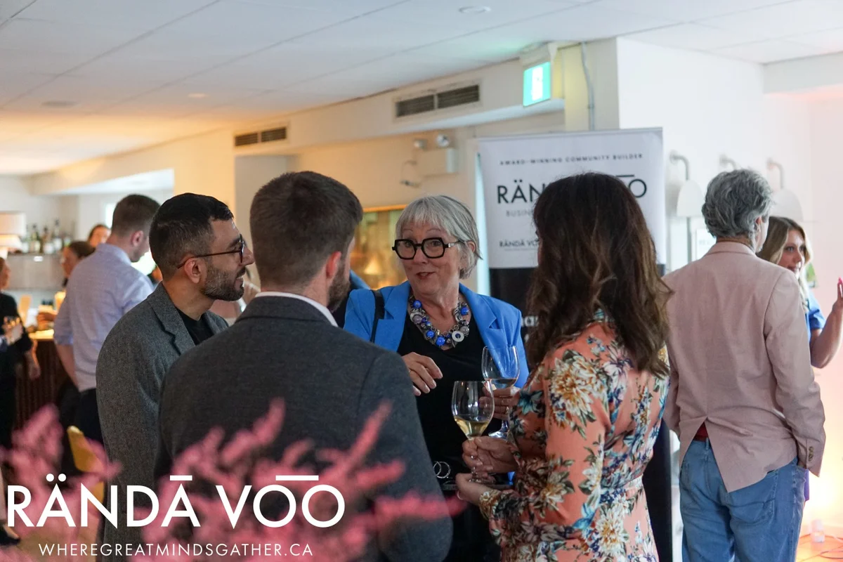 Guests gathered in conversation around a woman in a blue jacket, with RÄNDĀ VO͞O branding.