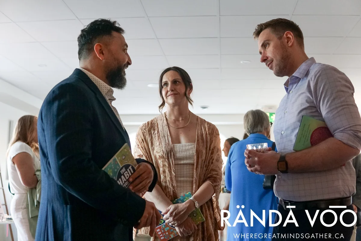 Three guests in conversation holding books and a drink at Parlour, with RÄNDĀ VO͞O branding.